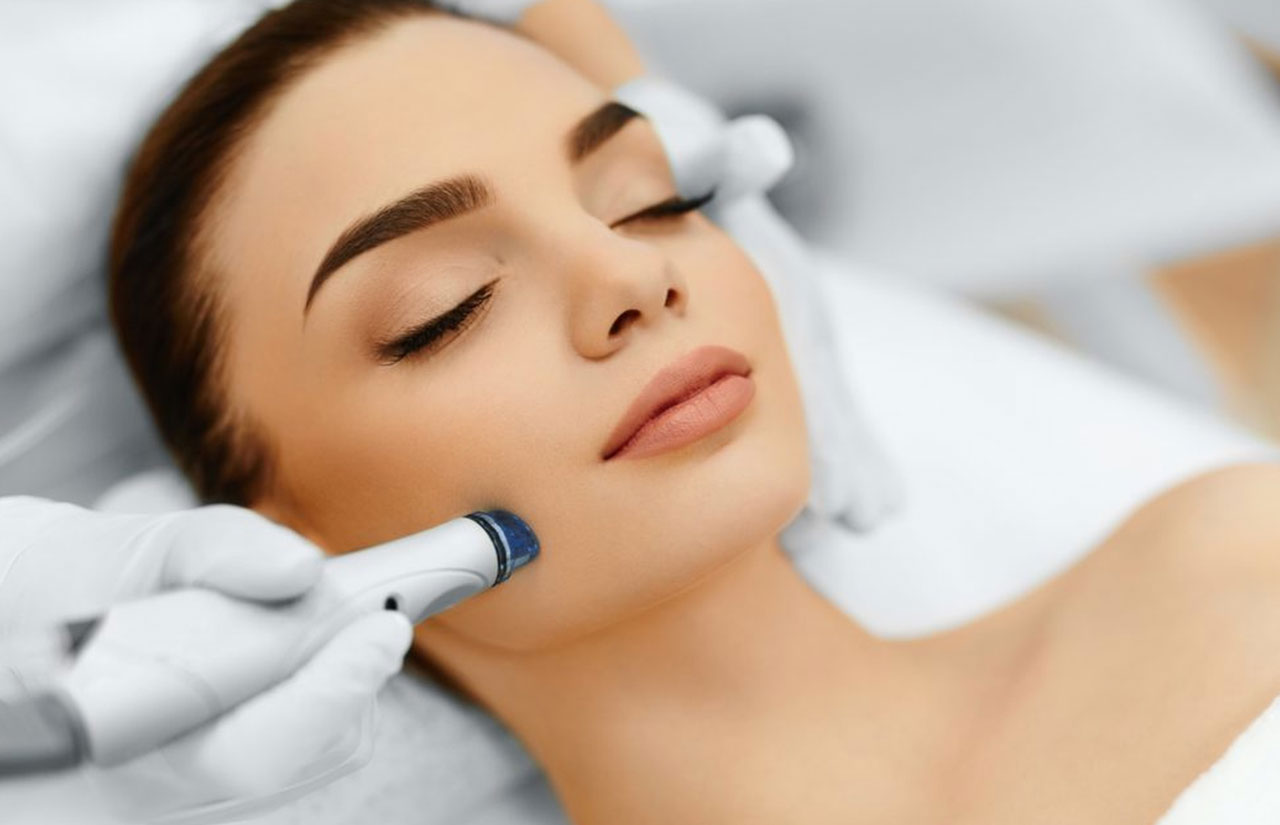 Makyajlı bir kadın ve yüzünde hydrafacial cihazı